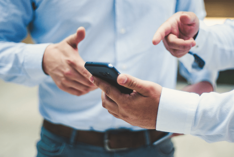 Datenerfassung im Vertrieb Ausschnitt von zwei Geschäftsleuten, die auf ein Handy zeigen