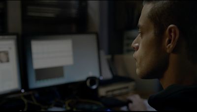 Rami Malek as Elliot Alderson, a cybersecurity engineer and hacker in Mr. Robot, sitting at a computer station with various screens.