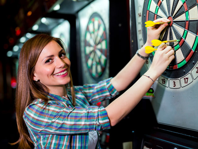 A woman pulling the darts she threw out of the dartboard.