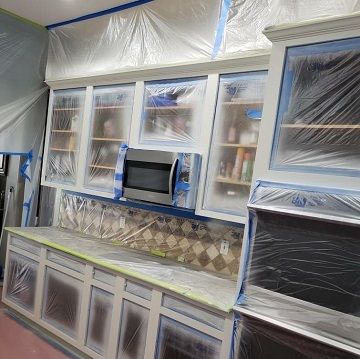 in progress picture of kitchen cabinets and appliances covered in plastic with tape