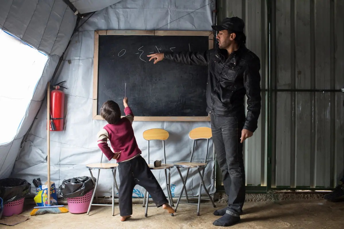 Syrian refugee Ayham* 28, points at the number 4, written in Arabic, on the blackboard as a student counts from 1 to 5, during a non-formal education program in Akkar, northern Lebanon