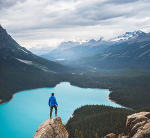 A man high up on a rock overlooking a bright green-blue lake in the mountains