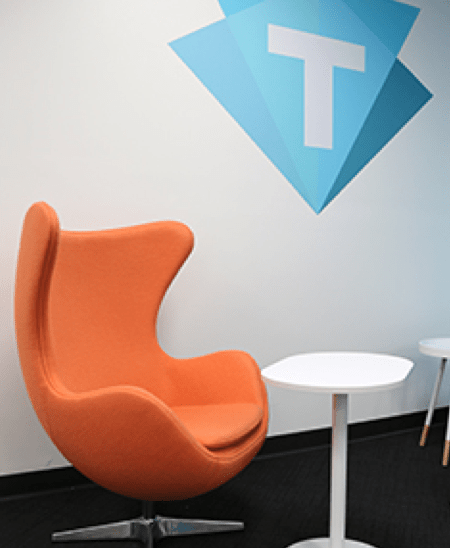 Orange chair with the Trilogy company logo on the wall above it