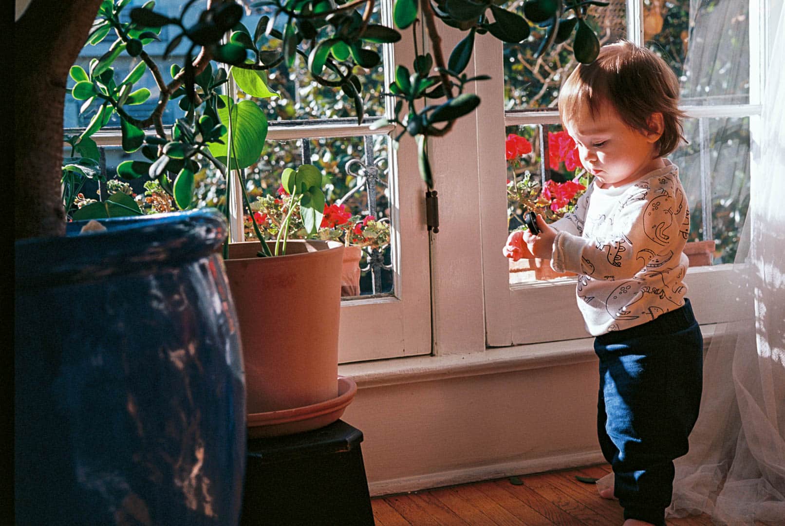 A baby standing next to a window as the sun streams in