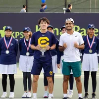 The mens' singles champion and finalist stand on the court with the trophies in front of the ball crew