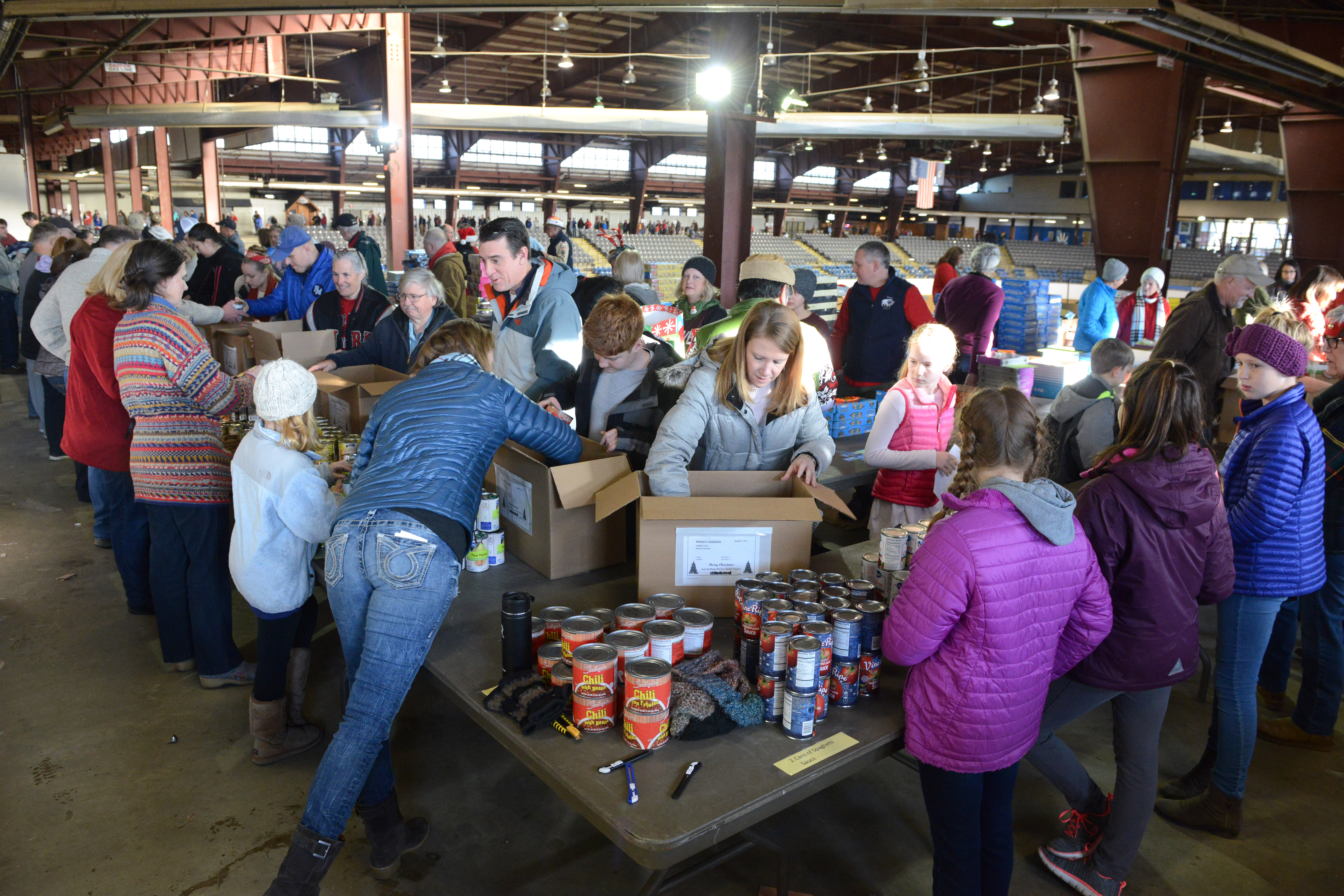 Big group of volunteers, young and old, dressed warmly, working together to pack canned goods into boxes.
