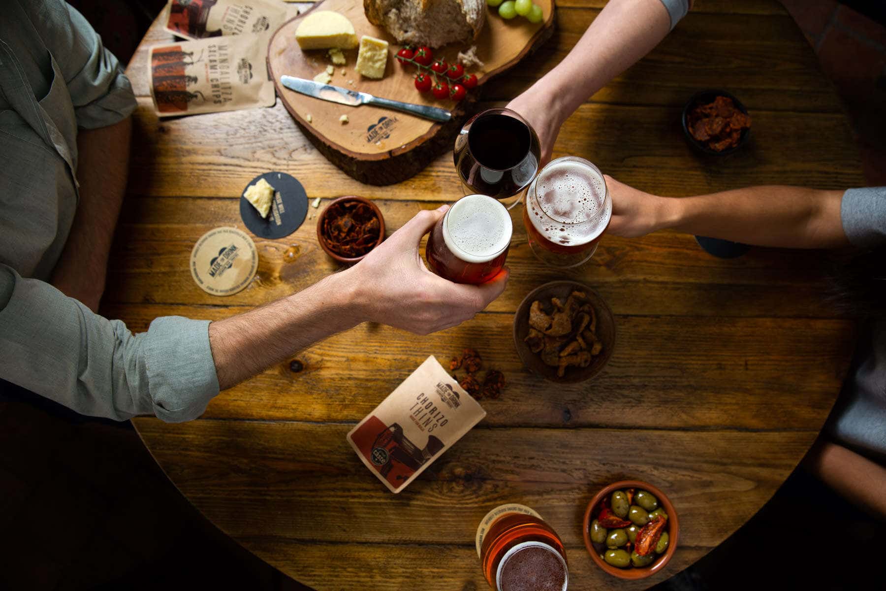 people clinking glasses in a bar over a table with a selection of nibbles on the table.