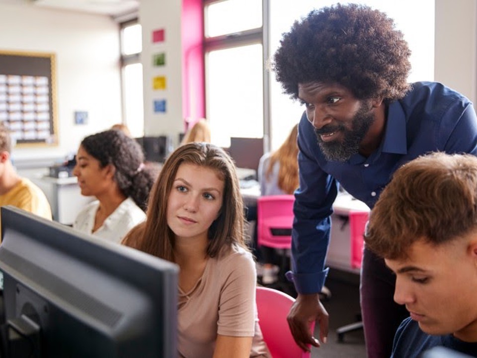 A teacher helps a student with a computer lesson.