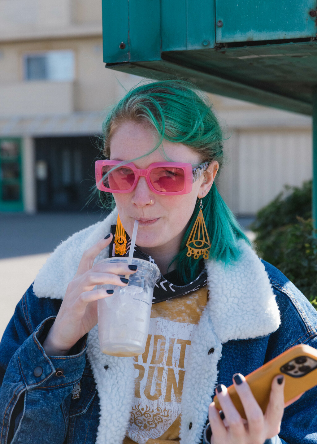 Beth's drinking an iced oat chai, wearing a yellow shirt, yellow earrings, and holding a yellow phone case