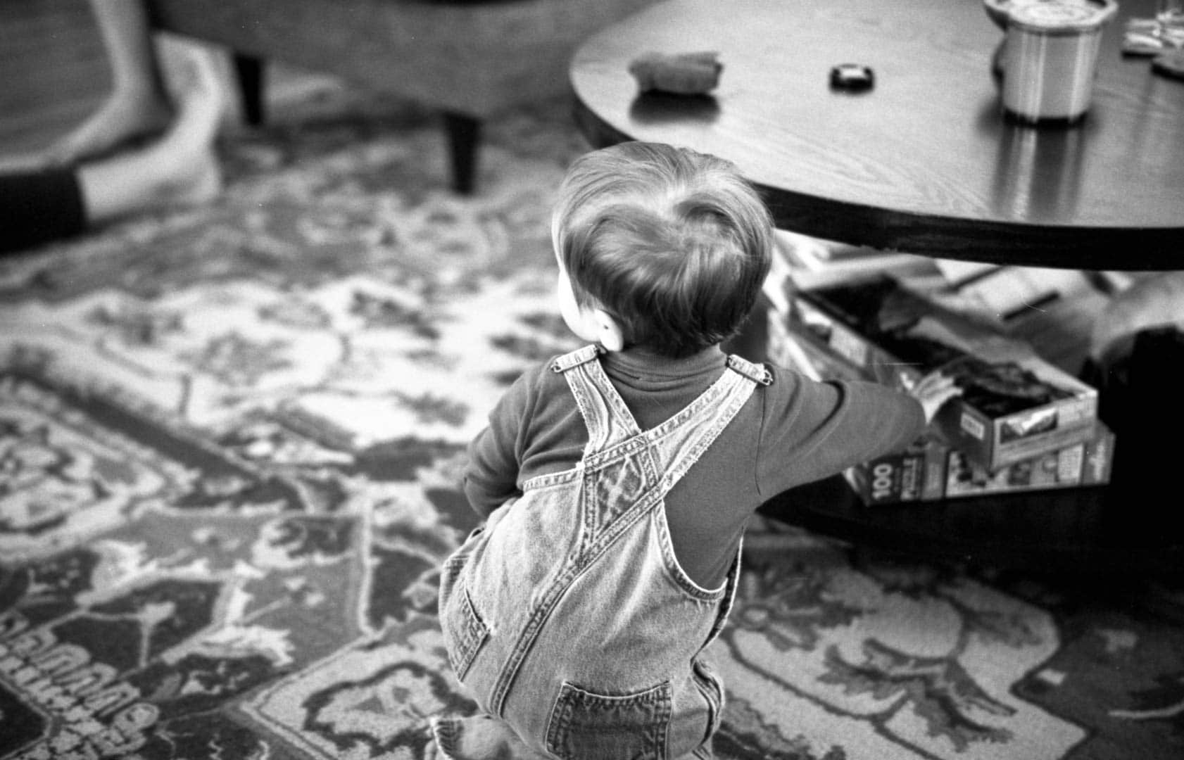 A baby in overalls plays on a living room floor