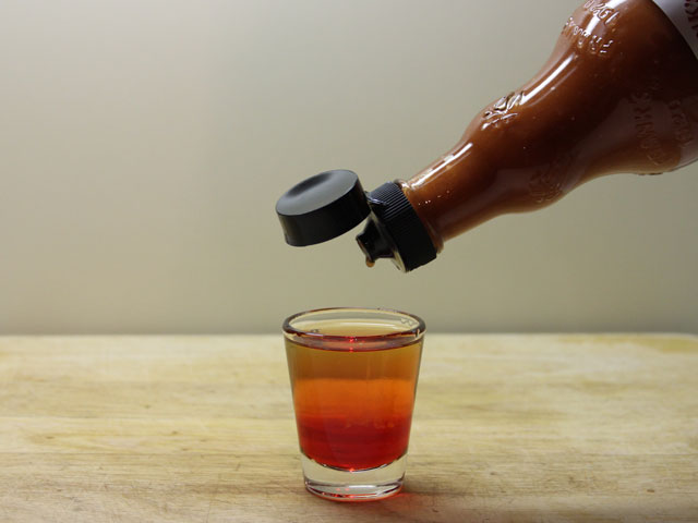 Adding 3-5 drops of hot sauce to a shot glass filled with grenadine and 151 rum