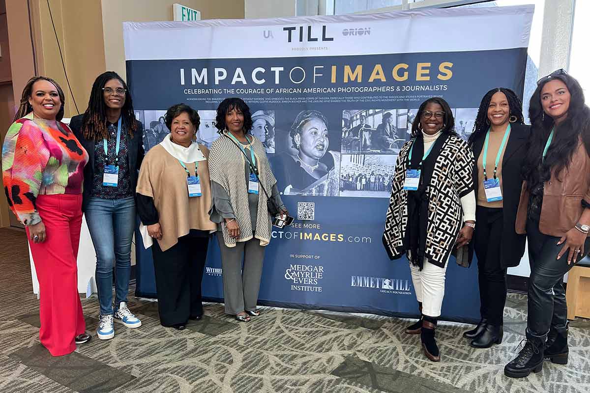 Image of people standing in front of an “Impact of Images” banner. Group includes Karuana Gatimu, Alexia Clayborne, Reena Evers Everette, Deborah Watts, Rosalind Withers, Teri Watts, and Natasha Bell.