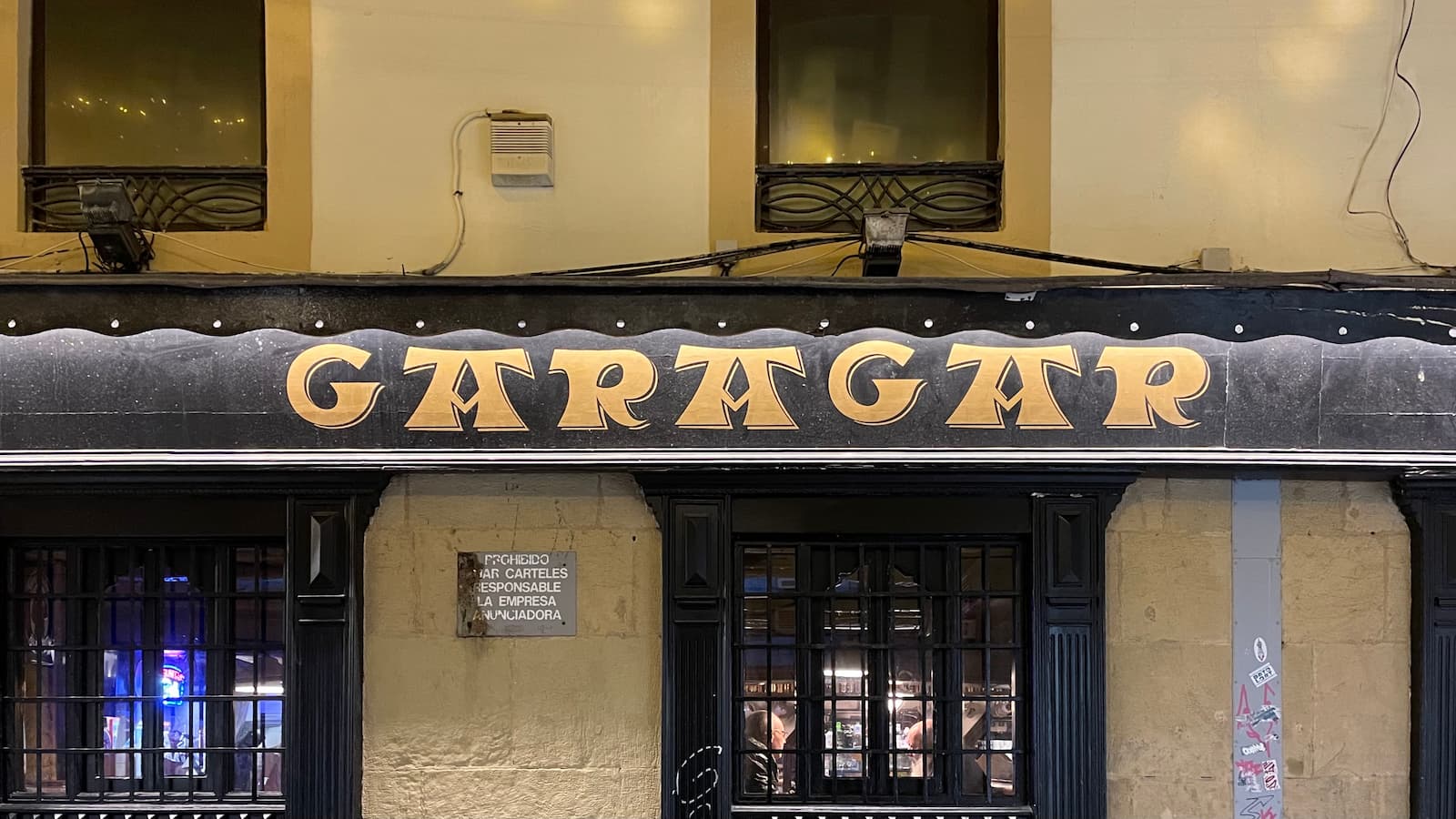 A storefront sign written in Basque with large, bold gold letters on a black background. The A characters have a crossbar on top, a bit like a hat.