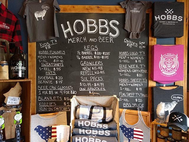 Hobbs Tavern merch, including shirts, growlers, six packs, kegs, and koozies
