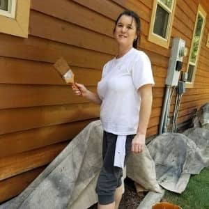woman painting the side of a wooden siding home