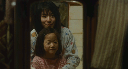 An animated gif of a scene from the film 'The Shoplifters' of a young woman and little girl happily practicing how to bow in the mirror.