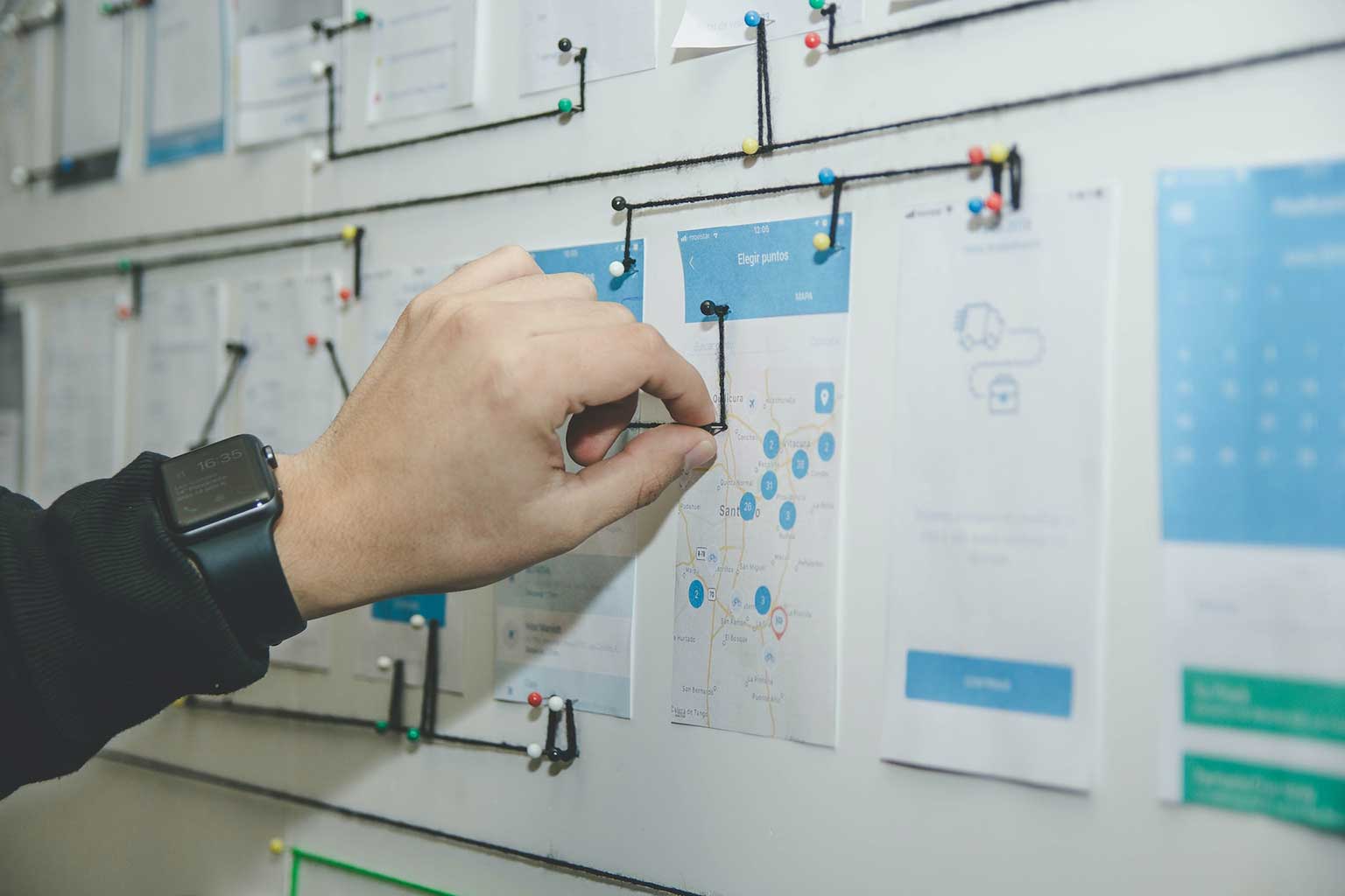 Printouts of a UI journey pinned to a wall and connected with strings, Photo by Alvaro Reyes on Unsplash