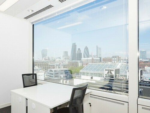 Simple shared workspace featuring white table with black office chairs and large window offering London city skyline views Google Meet background