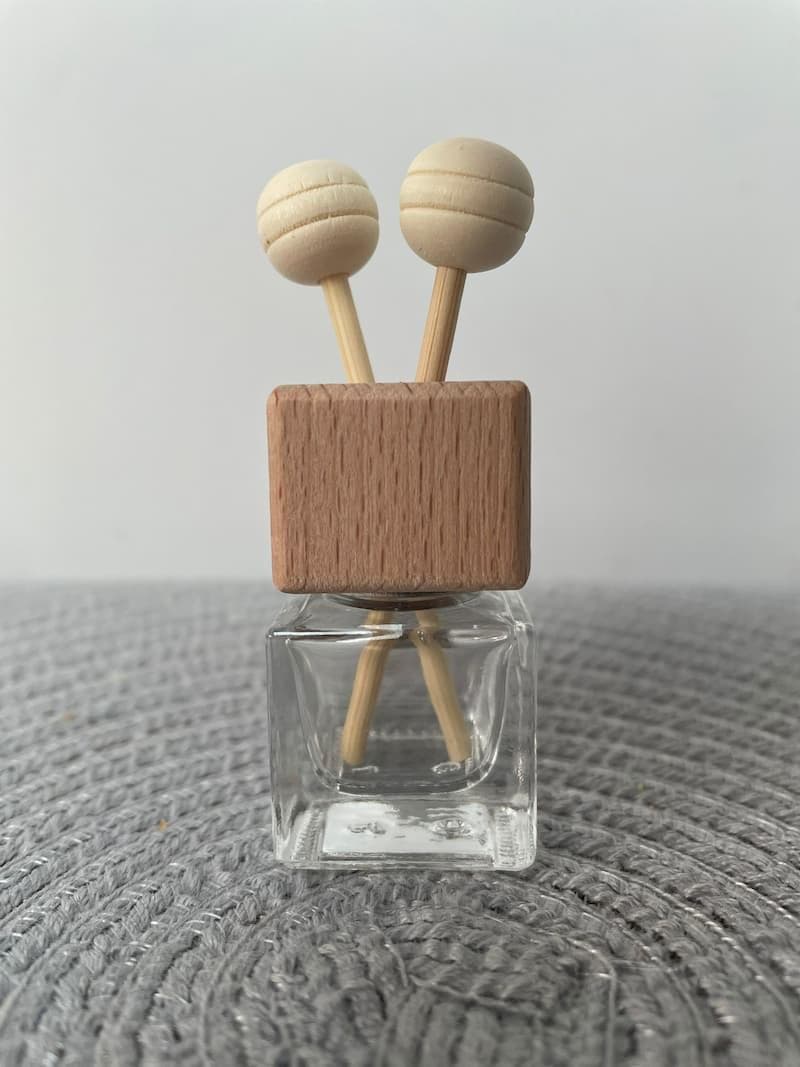 Glass bottle with wooden reed style screw lid and vent clip.