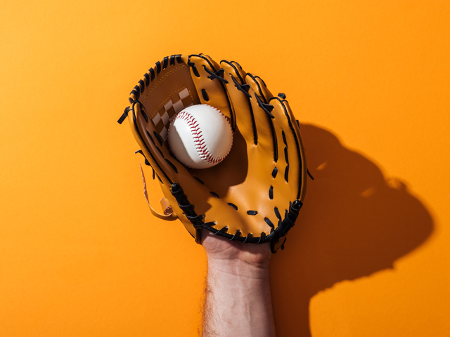 A baseball player catching a baseball with his glove with a gold background