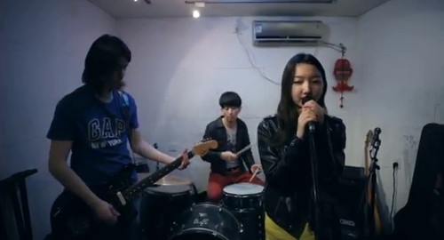A screenshot from the movie 'Follow Follow' showing Even singing with a band in a small rehearsal space.