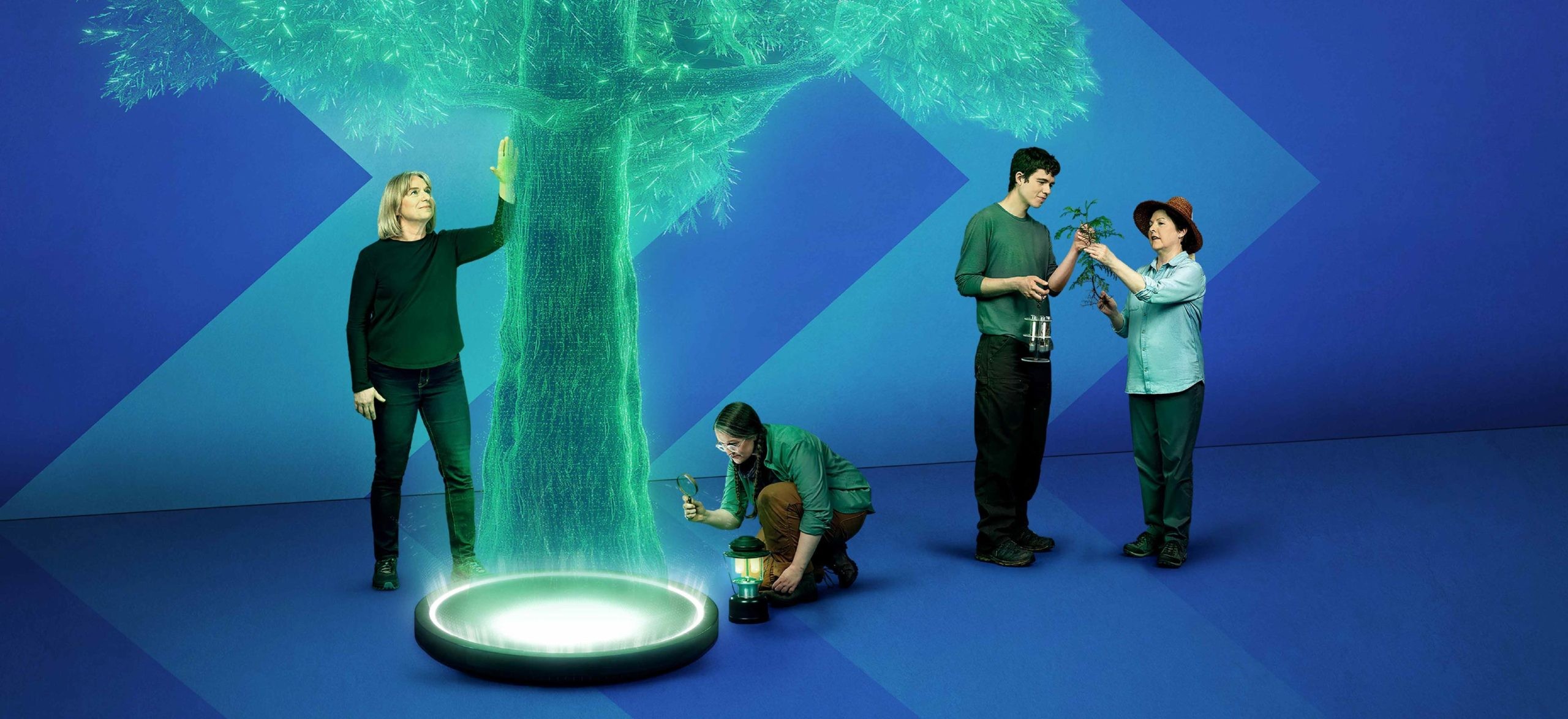 Dr. Suzanne Simard looks up at a green hologram of a tree while she places her hand on its trunk. UBC student Eva Snyder kneels down next to a lantern, inspecting the trunk with a magnifying glass. Hanno Southam and Dr. Teresa Ryan are standing to the right facing each other inspecting a small tree branch.