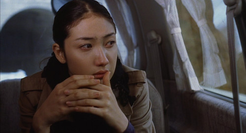 From the movie 'Pavillion Salamandre' a close-up screenshot of a woman Azuki (played by Yuu Kashii) looking out of a van window with her hands folded.