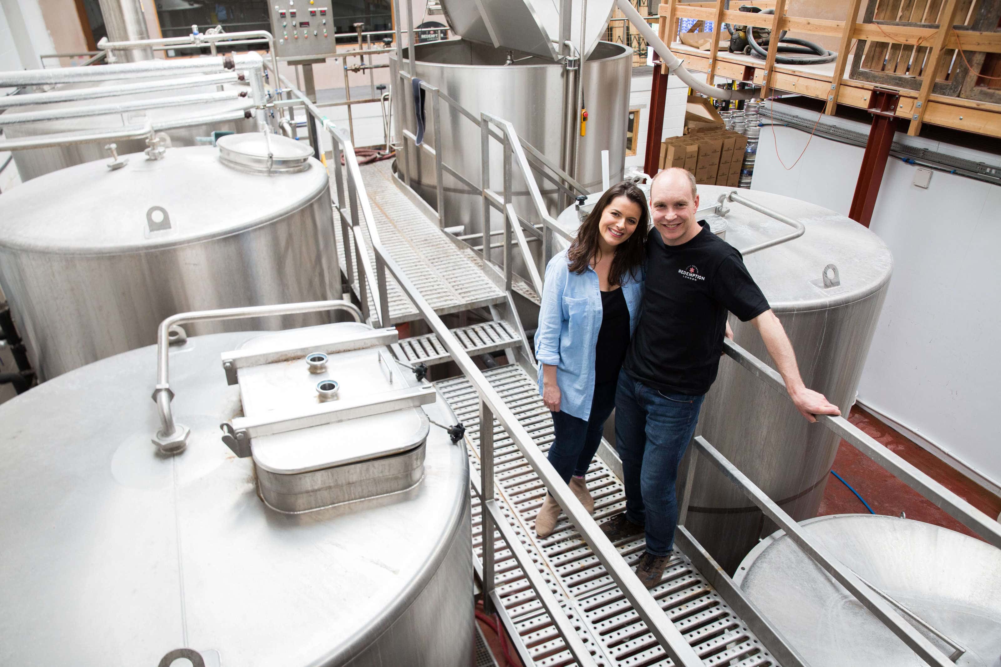 Portrait of Andy and Sam Rigby the owners or redemption brewery stood on the walk way above the beer vats in the brewery.