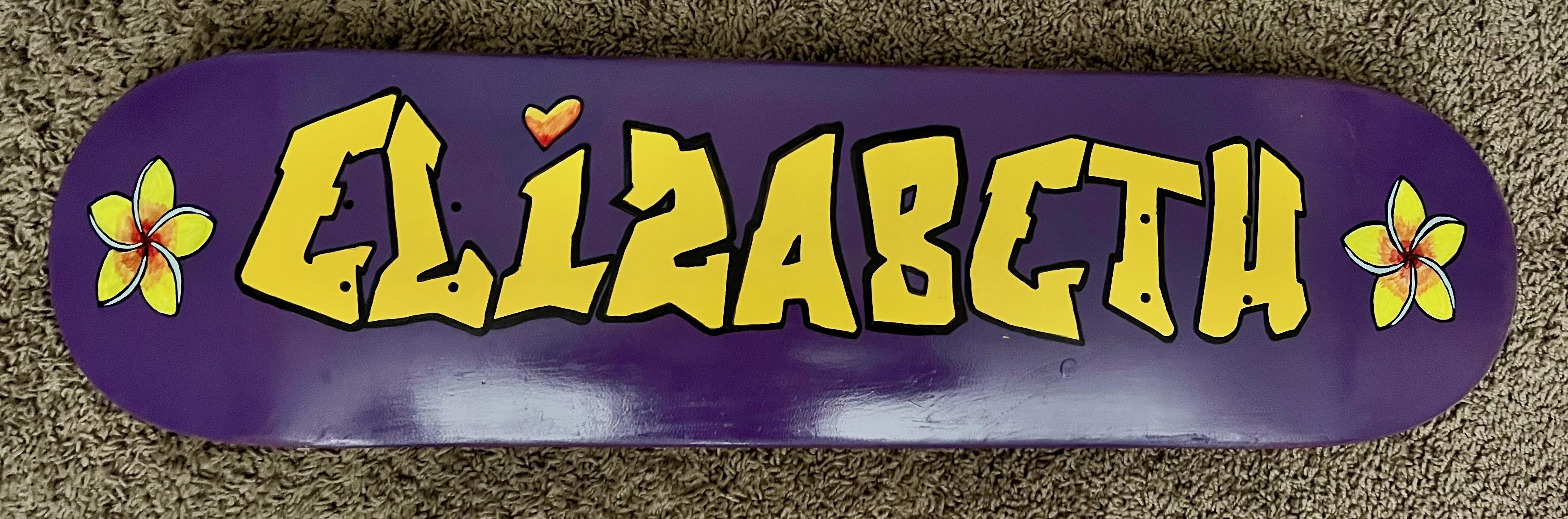 A photo of a skateboard deck with the name Elizabeth hand painted on it.