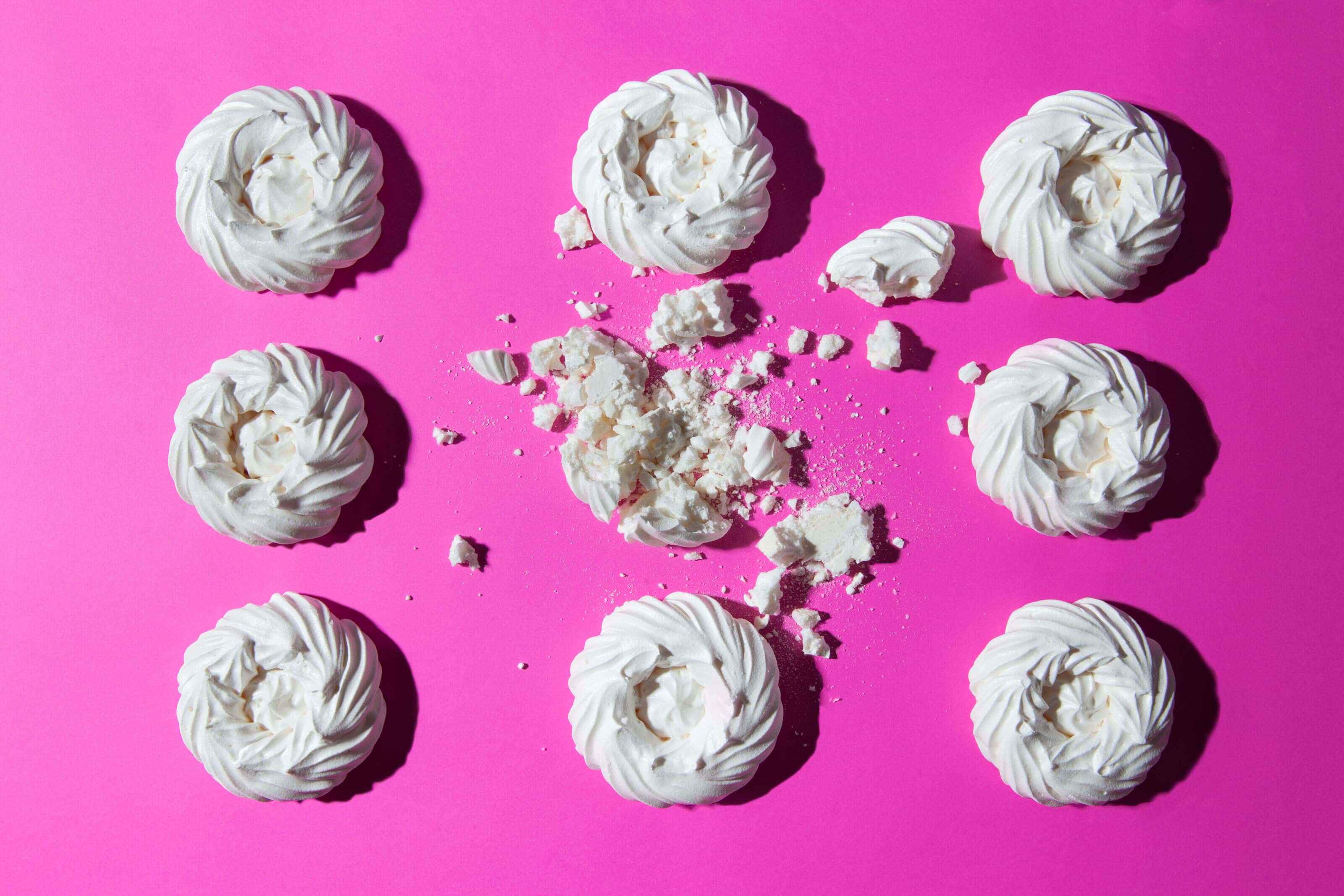 Meringue in a regular pattern on a pink background with one broken