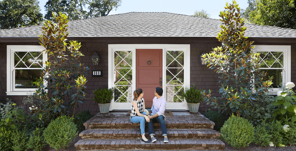 Young couple sitting on steps looking back at house.