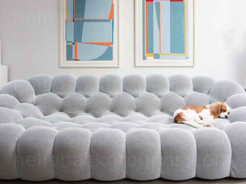 A small dog sleeping on a large grey sofa with modern bubble design in front of two wall mounted pieces of contemporary art  Skype background