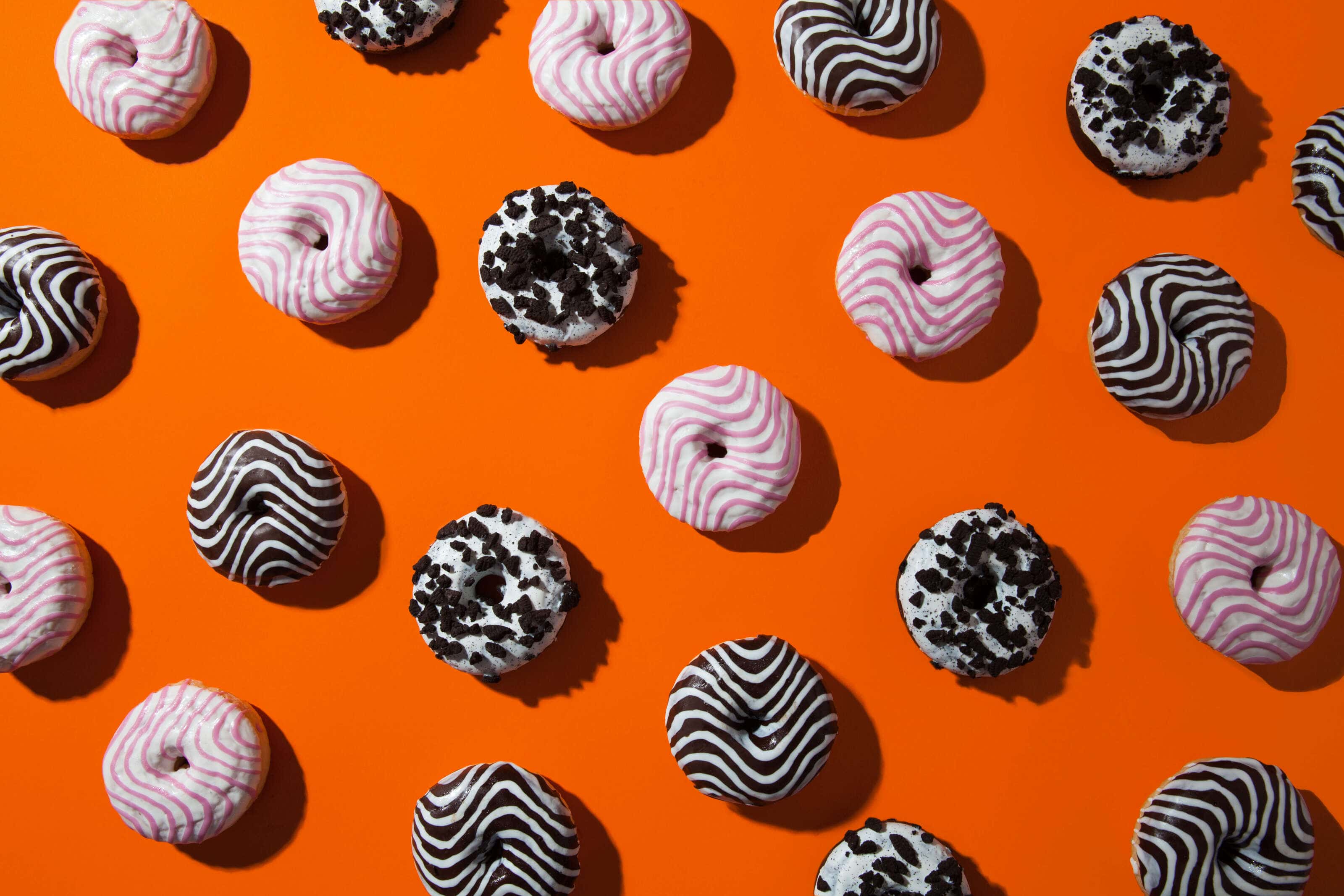 Doughnuts photographed on an orange background with hard shodows.