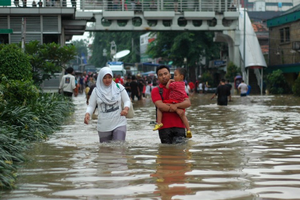 An Indonesian family wades through flood waters, part of a community that is affected by collective trauma after a natural disaster.