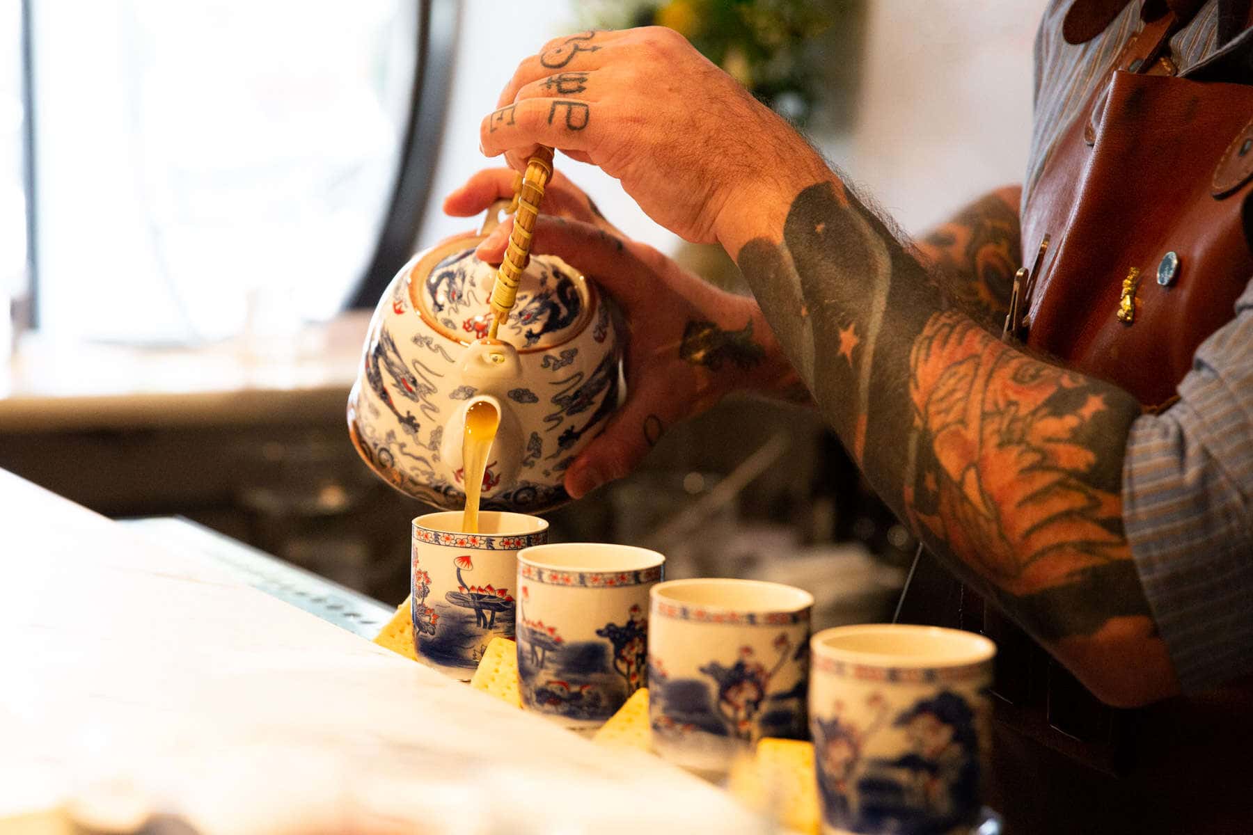 tea cocktail being pored by tattooed bartender