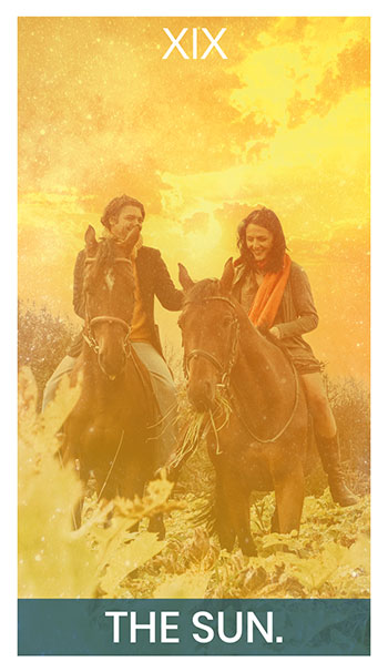 The Sun card. A couple riding horses in a golden field while smiling at eachother.