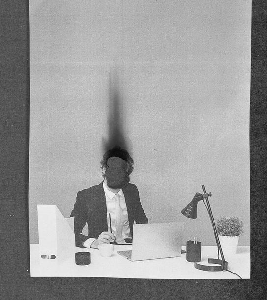 Ein Mann, der an einem Schreibtisch sitzt. Sein Kopf raucht.