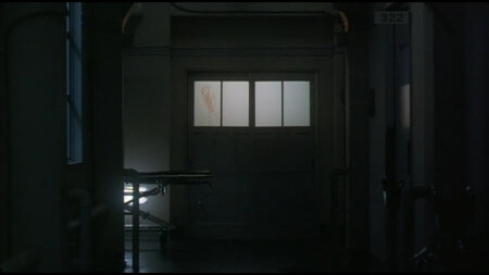 An ominous shot of a hospital corridor, with a set of double doors in the centre of the frame. The double doors have windows at about shoulder height, and one of the windows has a bloodied handprint smeared down it An ominous shot of a hospital corridor, with a set of double doors in the centre of the frame. The double doors have windows at about shoulder height, and one of the windows has a bloodied handprint smeared down it