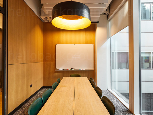 Compact boardroom with large exterior windows containing long wooden table and warm overhead lighting Microsoft Teams background