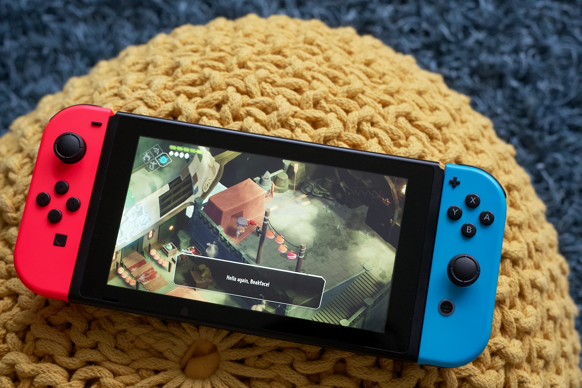 Nintendo Switch in handheld mode showing a game running. Two characters are having a conversation, a crow and a weird-looking guy with a pot as his head. Pothead says: Hello again, Beakface!