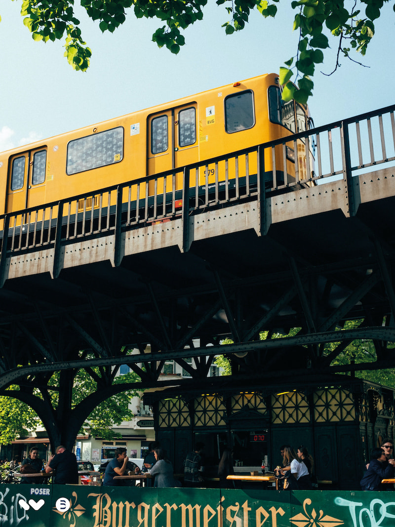 A yellow u-bahn train driving on a train track bridge in Berlin.