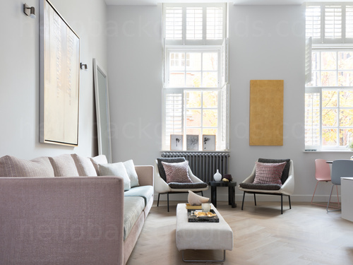 Large pastel coloured living room with high ceilings and large windows featuring large sofa with a footrest and 2 chairs Skype background