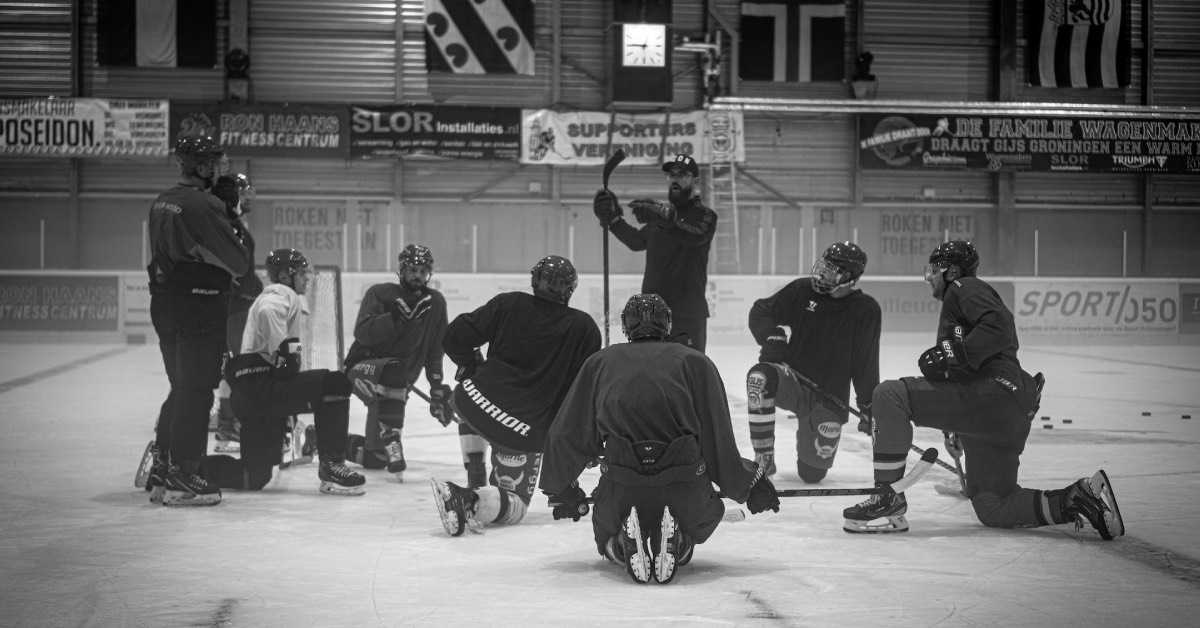 Ein Eishockey Team hat sich auf dem Spielfeld um den Trainer gruppiert und hört dessen Anweisungen zu, Foto in schwarz-weiß
