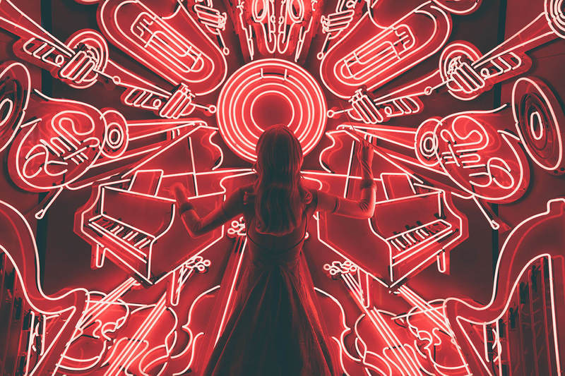 Uma garota de costas, olhando para uma parede cheia de LEDs em formatos de instrumentos musicais.