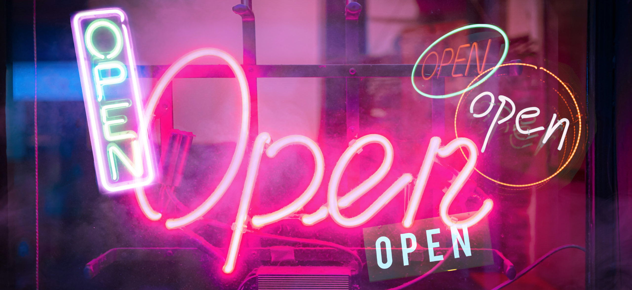 A photo illustration of several neon "Open" signs alight in the dark to signify re-opening of society after COVID-19
