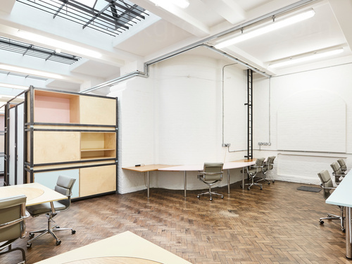 Spacious shared workspace with tiled wood floor featuring wood desks with chairs next to pastel multi-coloured cabinet  Zoom background
