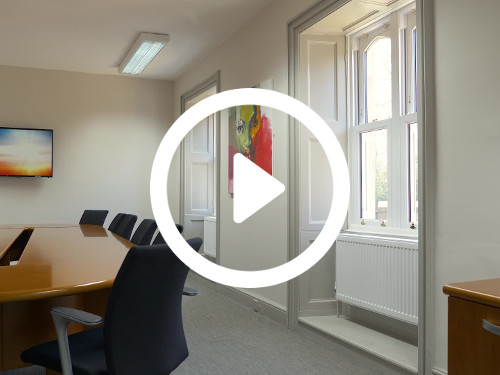Simple boardroom containing long wooden table with black office chairs nearby 2 abstract art pieces Zoom background