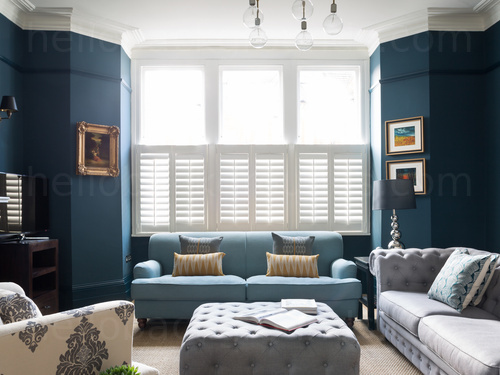 Light airy living room with dark blue walls featuring light pastel coloured sofas and prominent window Google Meet background