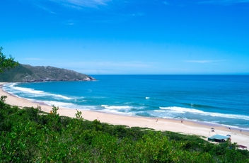 Vista da praia da Lagoinha do Leste, com par azul a direita e vegetação a esquerda. Ao fundo se vê o céu azul.