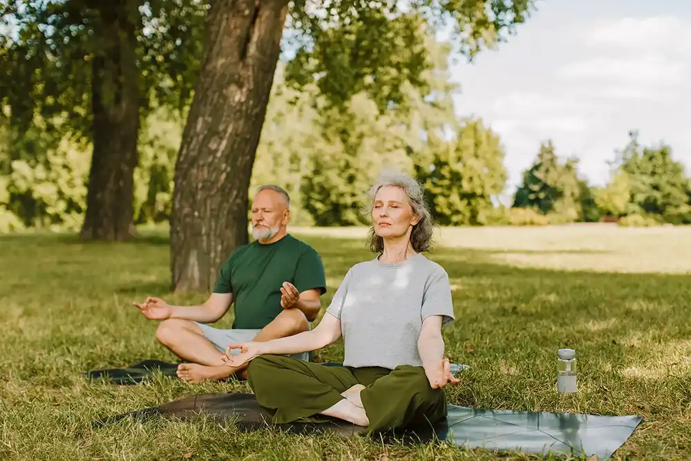 Mature woman and man meditating under a tree in a field